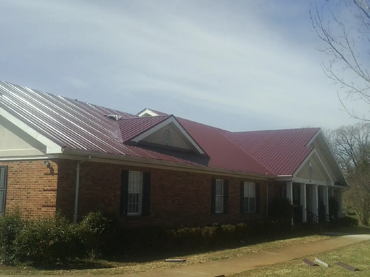 Red metal roof with gabled entries on a long brick building, from a Hail Damage Roof Repair job in Skokie