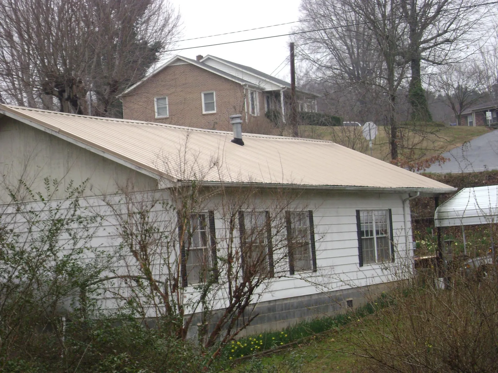 Tan metal roof on a white sided house set into a hillside — Commercial Roofing by Roofing Brothers in Skokie